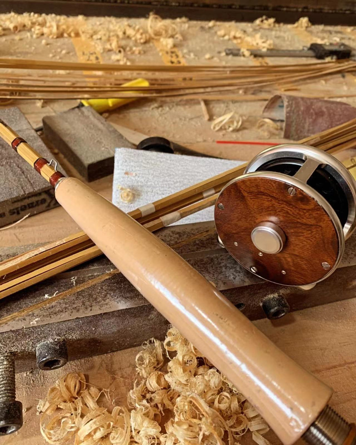 Bamboo fly rod, wooden fly reel and tools resting among cane shavings.