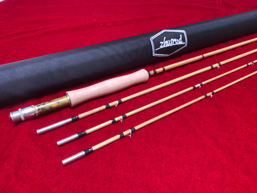 Bamboo fly rod sections and a ZHUSROD cloth rod bag on red fabric.