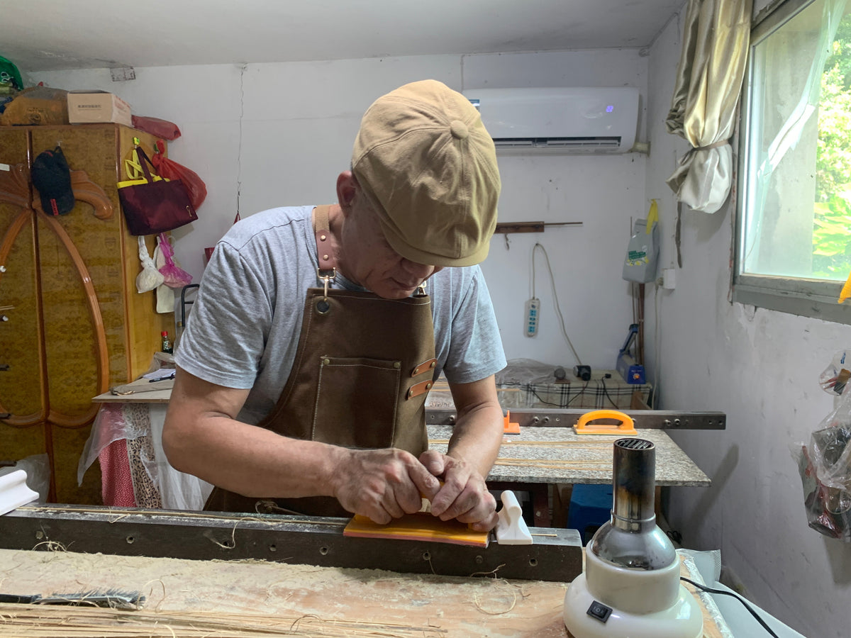 Rod maker working a bamboo strip with a hand plane at the bench.