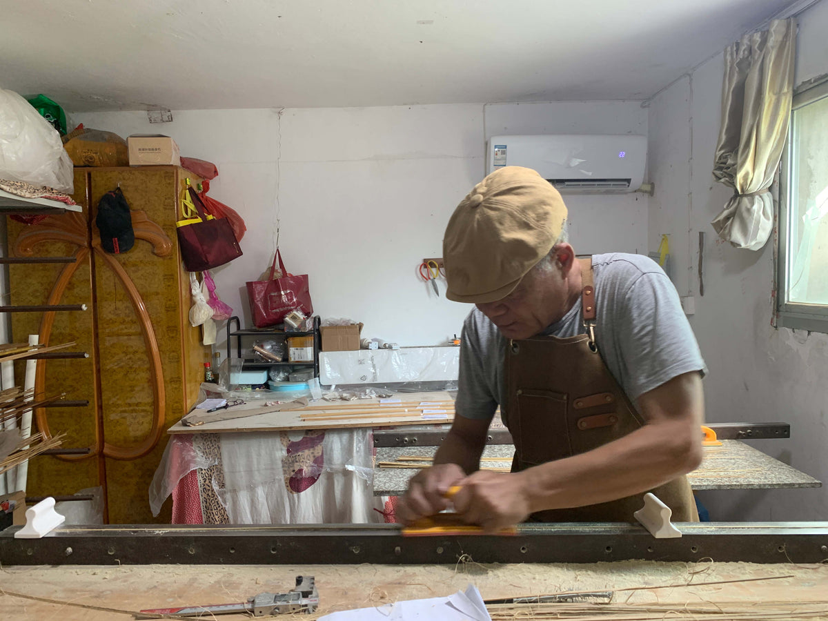 Rod maker working on a bamboo strip at a bench covered with shavings.