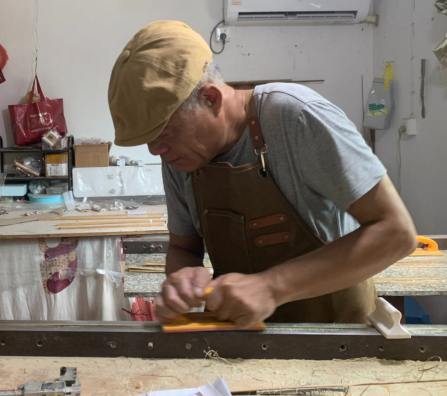 Rod maker hand-planing a bamboo strip at a workshop bench.