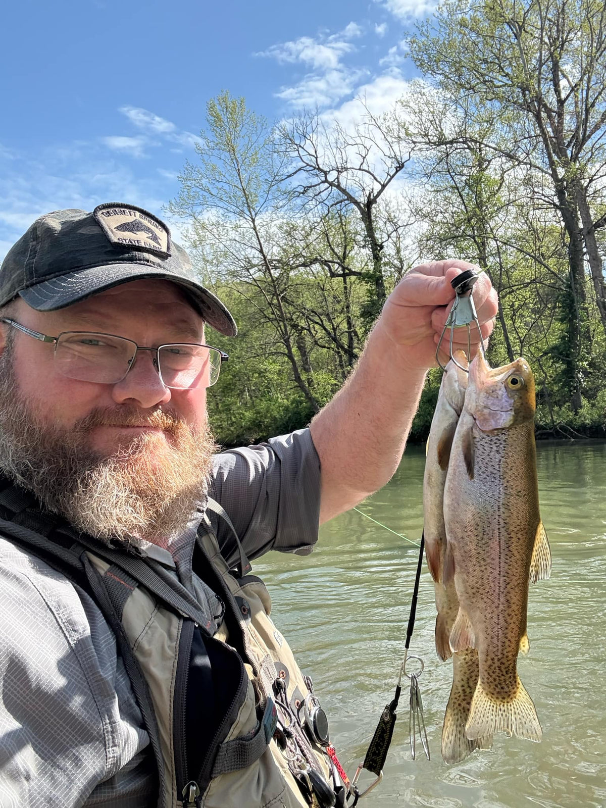 Angler holding two fish beside a river.