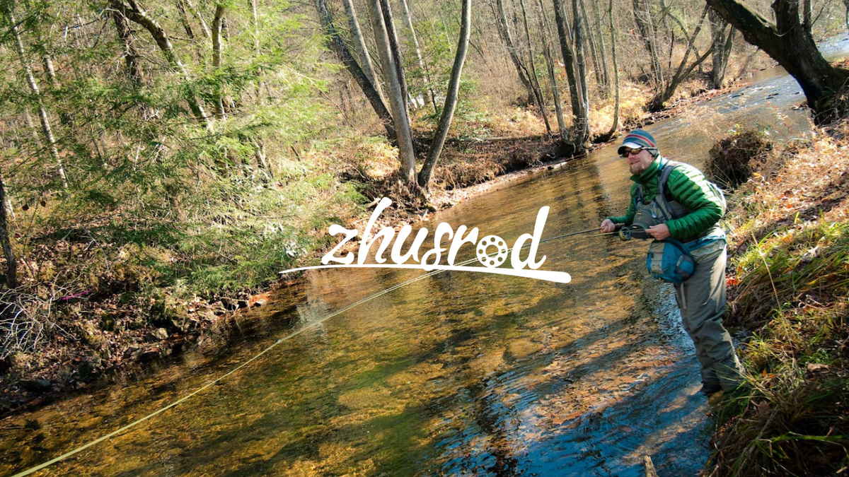 Angler wading and casting in a narrow wooded stream.
