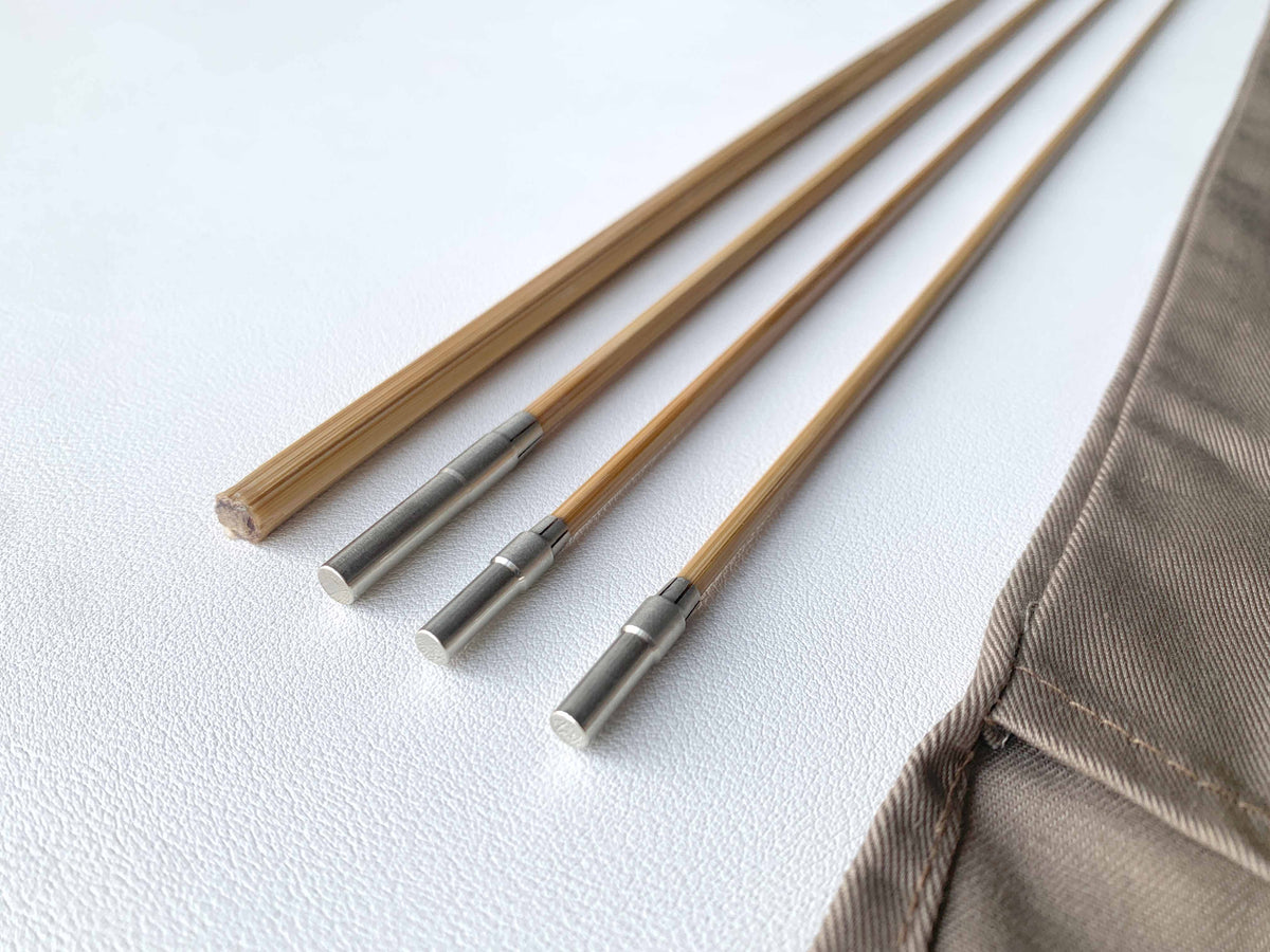 Bamboo rod blank sections with fitted metal ferrules beside a cloth bag.